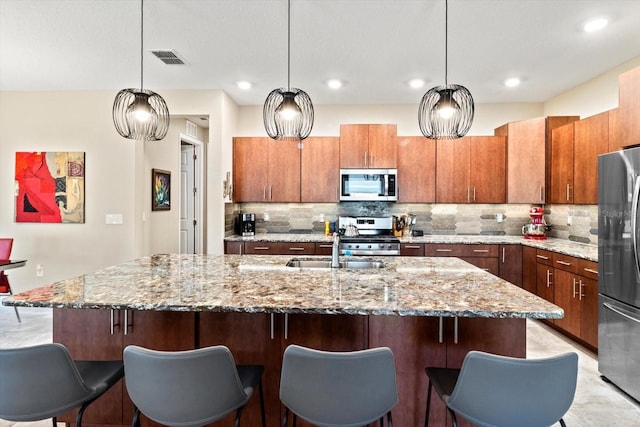 kitchen with light stone counters, decorative backsplash, brown cabinetry, and stainless steel appliances
