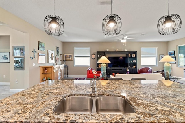 kitchen featuring stone countertops, a sink, pendant lighting, and open floor plan