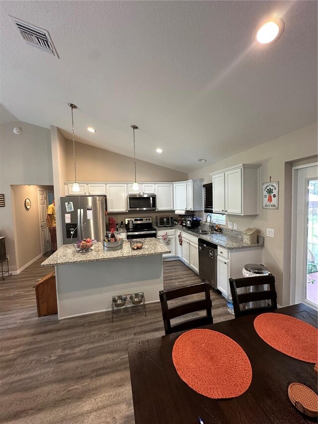 kitchen with visible vents, lofted ceiling, a kitchen island, white cabinets, and stainless steel appliances