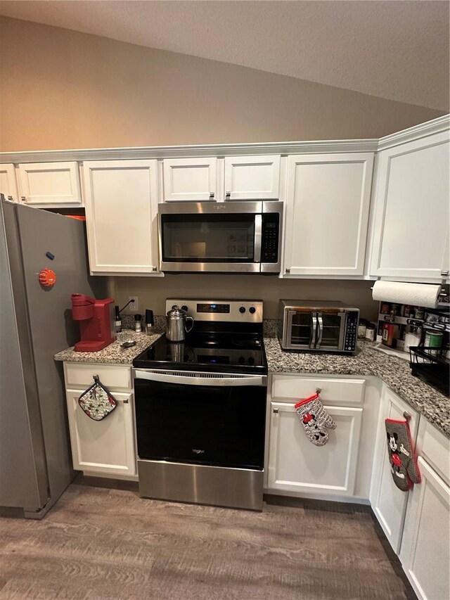 kitchen with a toaster, appliances with stainless steel finishes, white cabinets, and vaulted ceiling