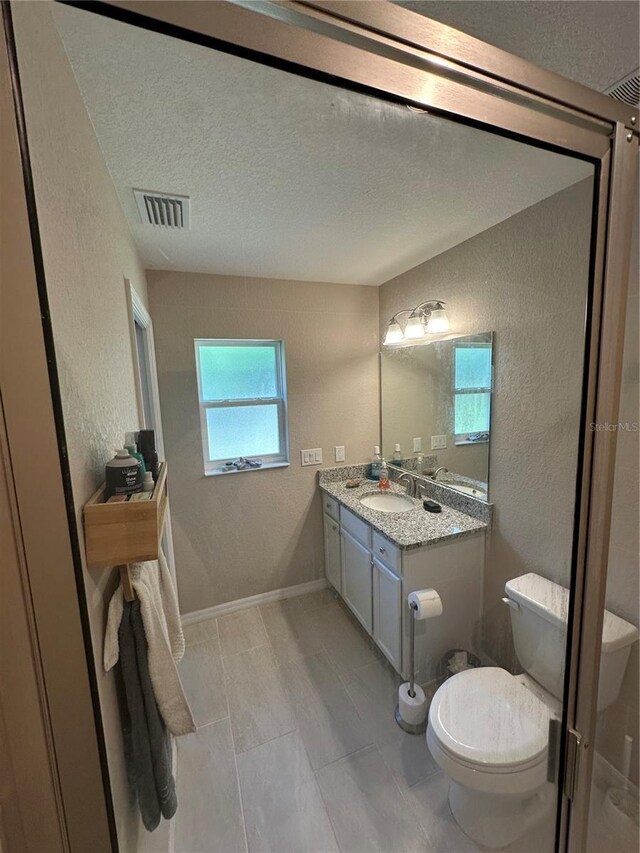 bathroom with visible vents, a textured ceiling, and a textured wall