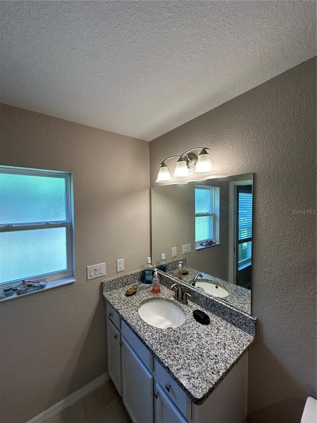bathroom with a textured ceiling, a textured wall, tile patterned floors, and vanity