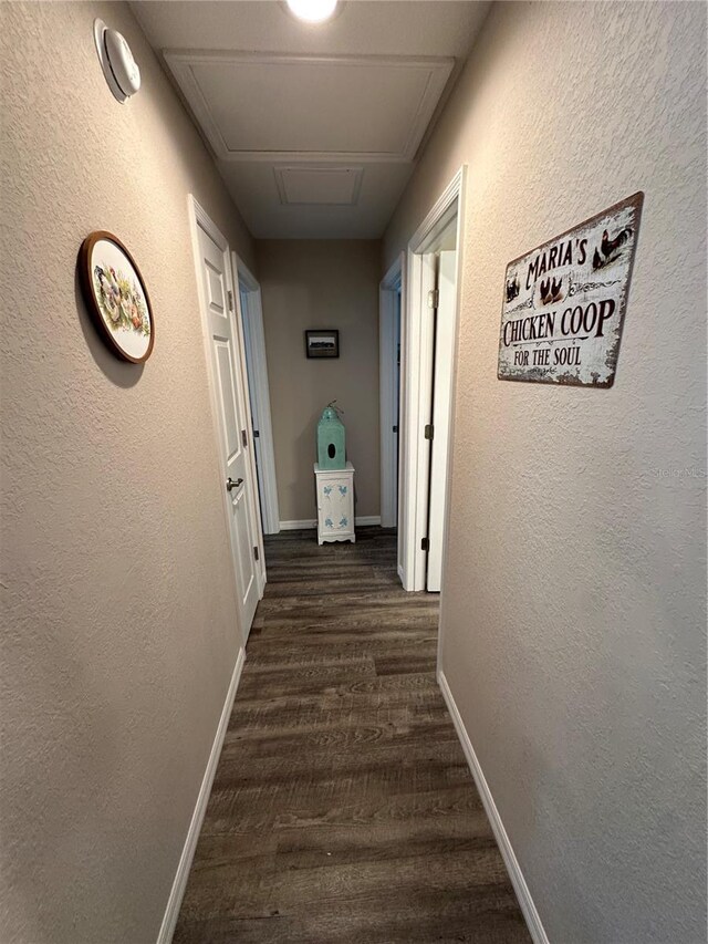 hallway with baseboards, a textured wall, attic access, and dark wood finished floors