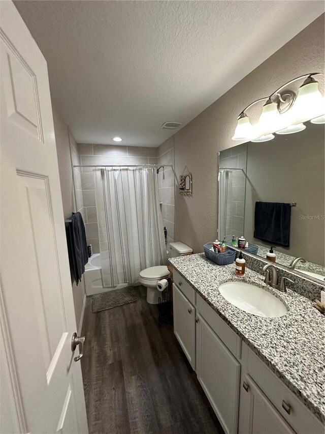 full bath with vanity, toilet, a textured ceiling, wood finished floors, and shower / tub combo