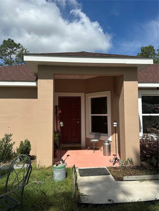 property entrance with a porch, roof with shingles, and stucco siding