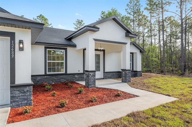 view of front of property featuring a shingled roof, stucco siding, and stone siding