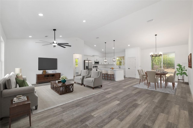 living area with light wood-style floors, high vaulted ceiling, ceiling fan with notable chandelier, and recessed lighting