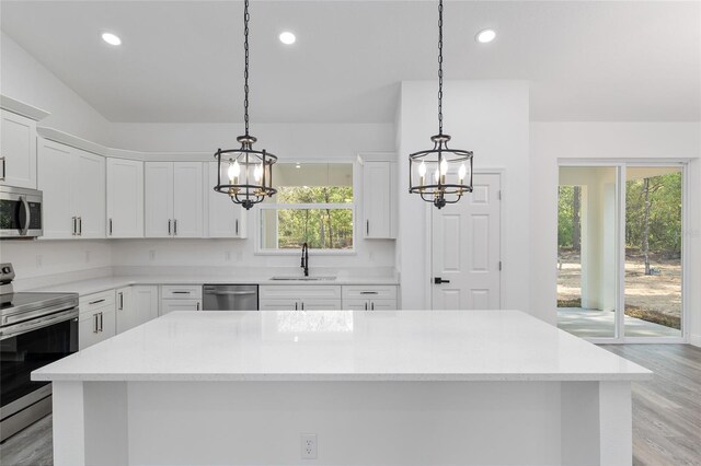 kitchen featuring white cabinets, a sink, light wood-style flooring, appliances with stainless steel finishes, and a notable chandelier