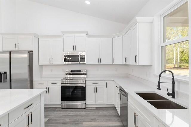 kitchen featuring white cabinets, appliances with stainless steel finishes, a sink, light wood-style floors, and vaulted ceiling