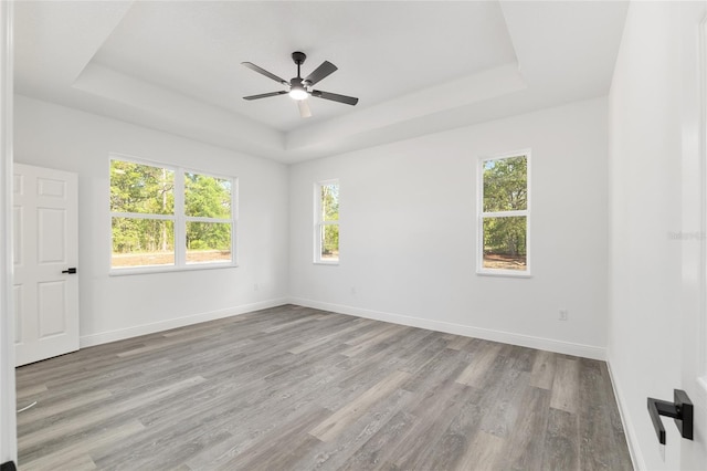 empty room featuring a healthy amount of sunlight, a raised ceiling, ceiling fan, and wood finished floors