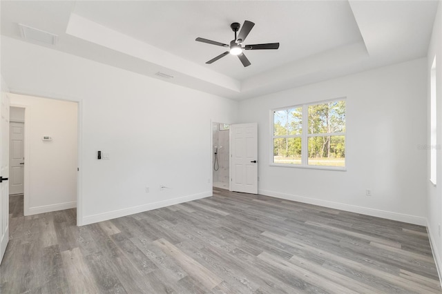 empty room with ceiling fan, visible vents, wood finished floors, baseboards, and a tray ceiling