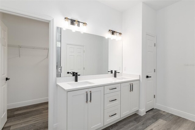 full bathroom featuring a sink, baseboards, double vanity, and wood finished floors