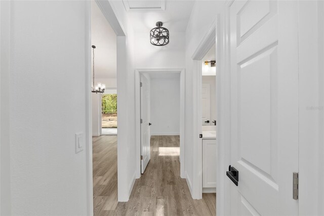 hall featuring light wood-style floors, baseboards, and a chandelier