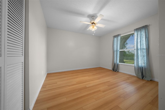 spare room with light wood-style floors, baseboards, a ceiling fan, and a textured ceiling