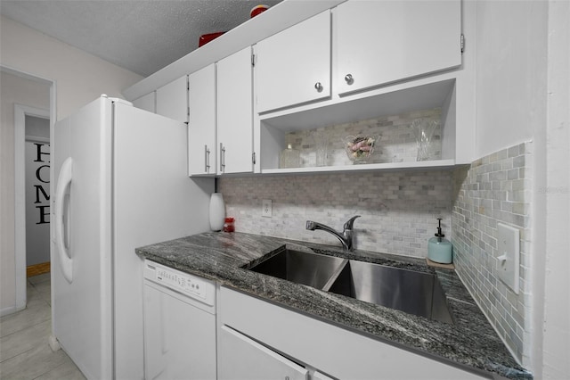 kitchen featuring backsplash, white dishwasher, open shelves, a sink, and dark stone counters
