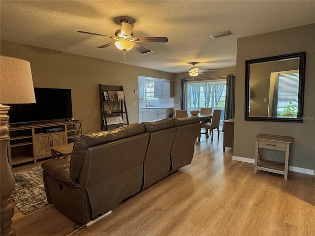 living area with ceiling fan, light wood-style flooring, and visible vents