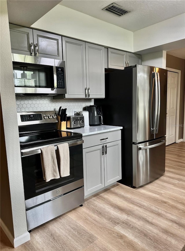 kitchen featuring gray cabinets, backsplash, visible vents, light wood-type flooring, and stainless steel appliances