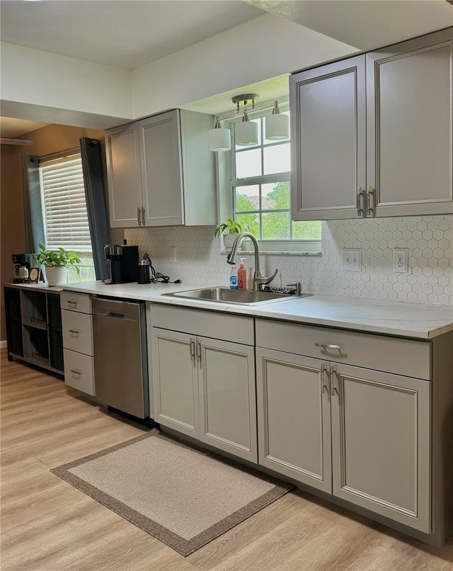 kitchen with a sink, dishwasher, light countertops, gray cabinets, and light wood-style flooring