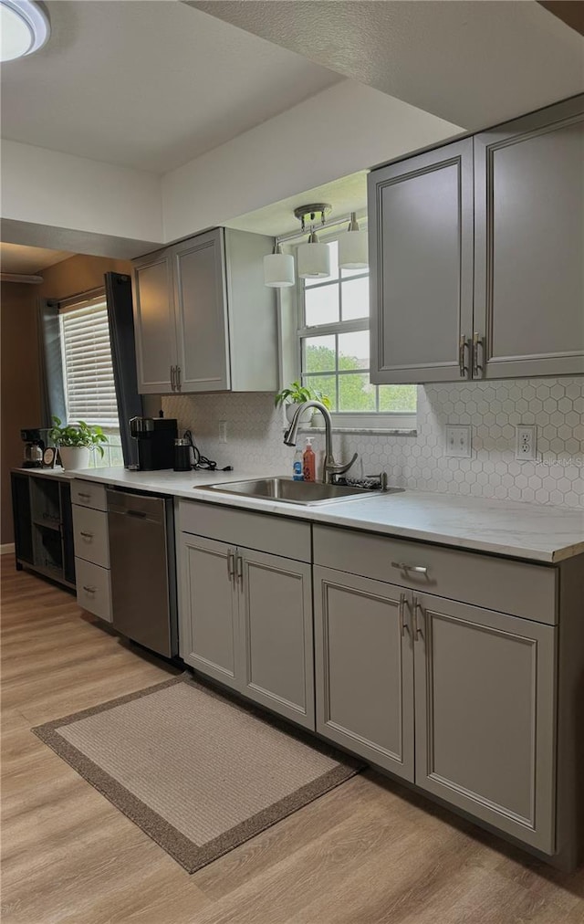 kitchen with a sink, light wood finished floors, dishwasher, gray cabinets, and a wealth of natural light