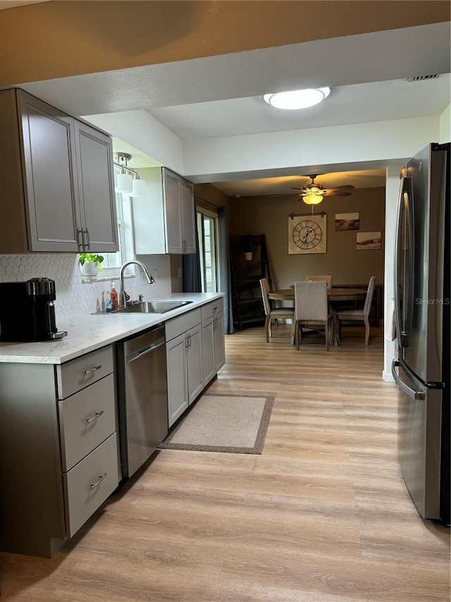 kitchen with gray cabinets, a sink, light countertops, stainless steel appliances, and light wood-style flooring