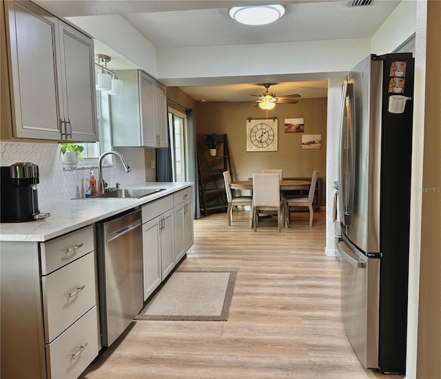kitchen featuring appliances with stainless steel finishes, a sink, light countertops, light wood-style flooring, and gray cabinetry