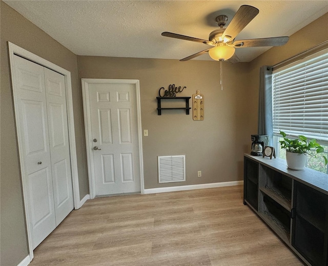 interior space with ceiling fan, a textured ceiling, visible vents, baseboards, and light wood finished floors