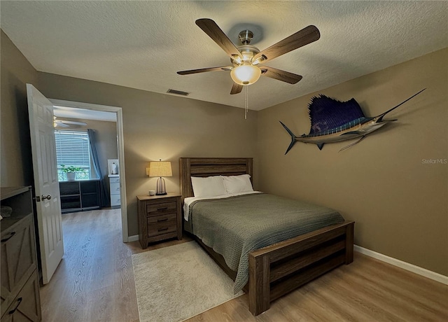 bedroom featuring light wood-type flooring, a textured ceiling, baseboards, and visible vents