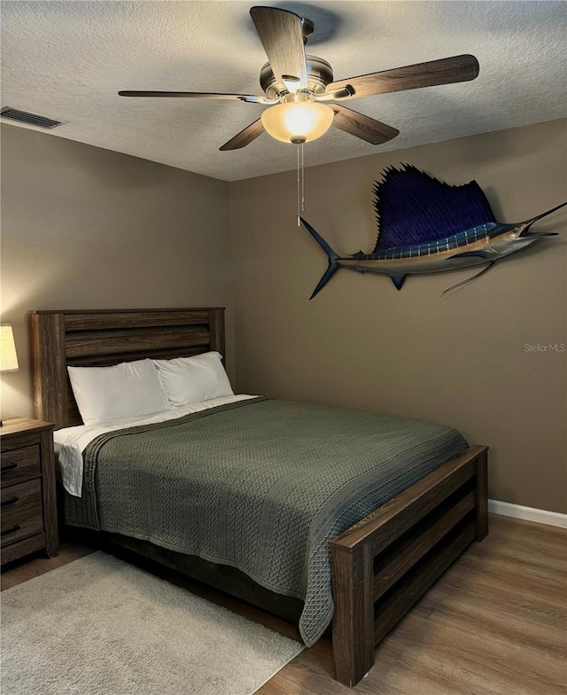 bedroom with visible vents, wood finished floors, baseboards, a textured ceiling, and a ceiling fan