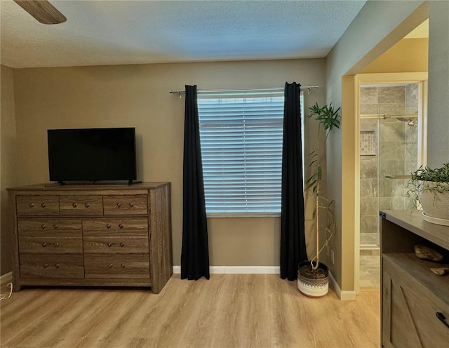 bedroom featuring baseboards, light wood-type flooring, a textured ceiling, a ceiling fan, and ensuite bath