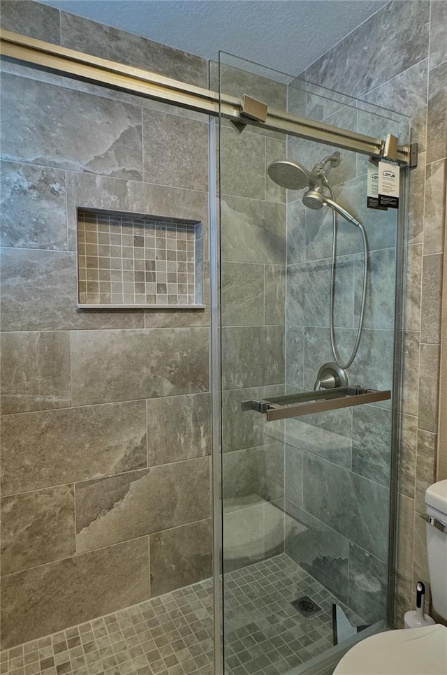 full bath with a textured ceiling, toilet, and a shower stall