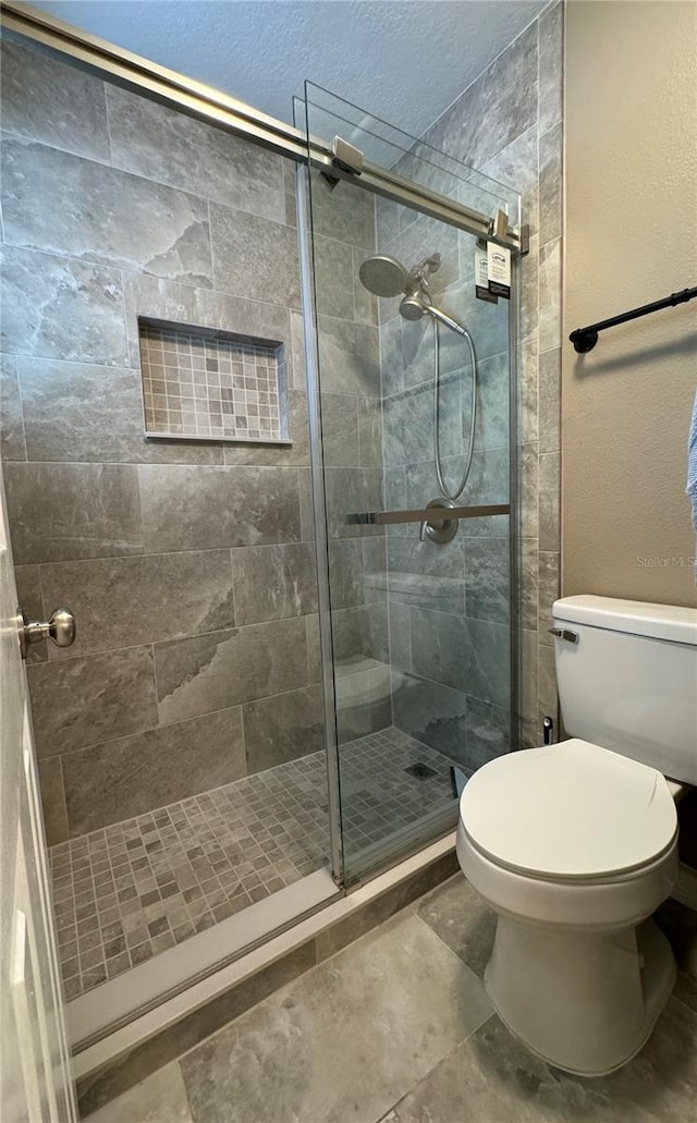 full bathroom with toilet, a textured ceiling, and a shower stall