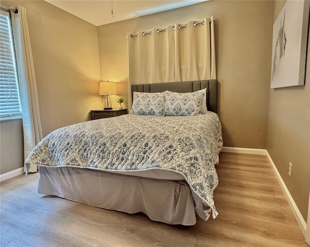 bedroom with baseboards, multiple windows, and wood finished floors