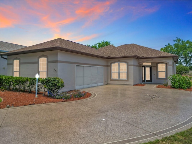 view of front of property with an attached garage, roof with shingles, stucco siding, and concrete driveway