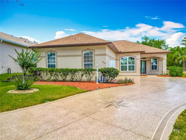 mediterranean / spanish-style house featuring roof with shingles, stucco siding, and a front yard