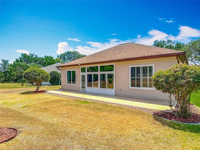 rear view of property featuring a lawn, stucco siding, and roof with shingles