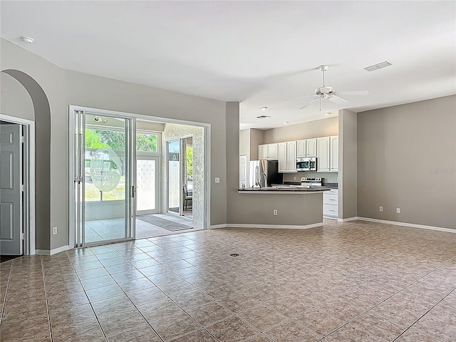unfurnished living room with visible vents, arched walkways, baseboards, and ceiling fan