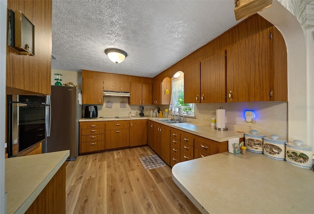 23737 NW Mallard Ave, Dunnellon, FL 34431 - kitchen featuring freestanding refrigerator, under cabinet range hood, brown cabinets, light countertops, and oven