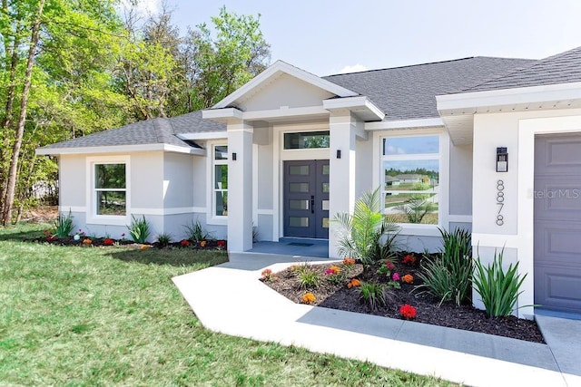 doorway to property featuring a yard, stucco siding, and roof with shingles
