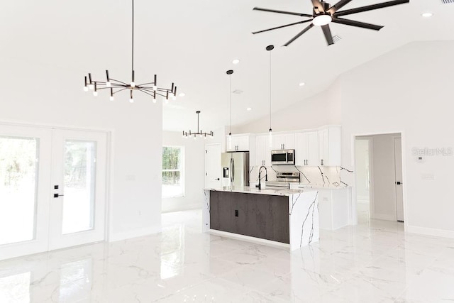kitchen featuring decorative light fixtures, white cabinetry, high vaulted ceiling, stainless steel appliances, and an island with sink