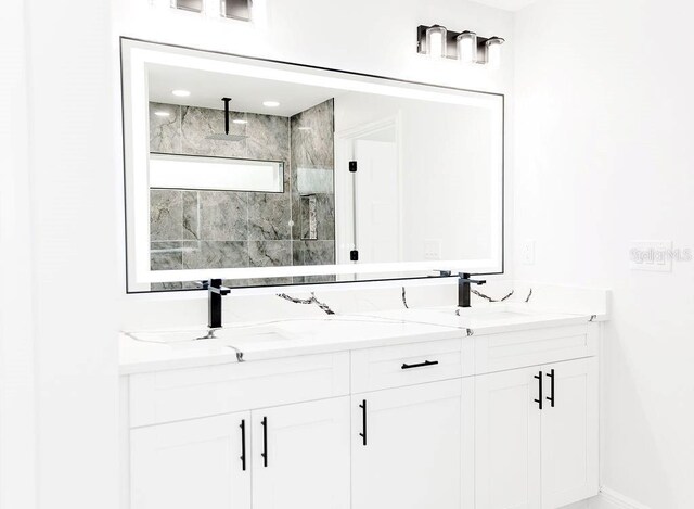 full bath with baseboards, walk in shower, double vanity, and a sink