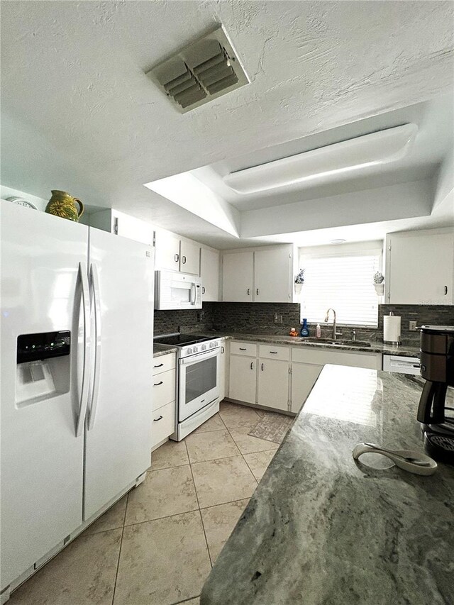 kitchen featuring visible vents, decorative backsplash, white appliances, a tray ceiling, and a sink