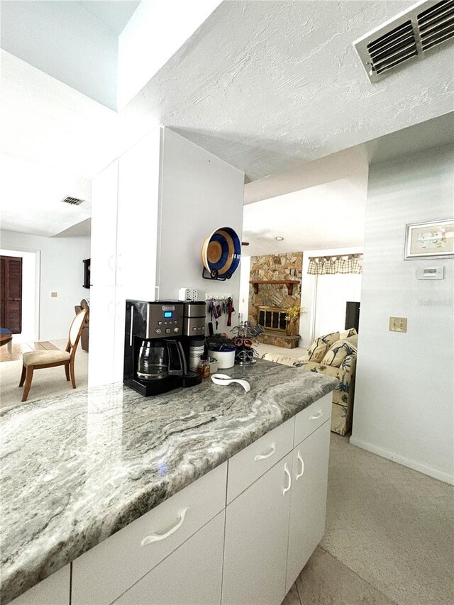 kitchen featuring white cabinetry, baseboards, visible vents, and a fireplace