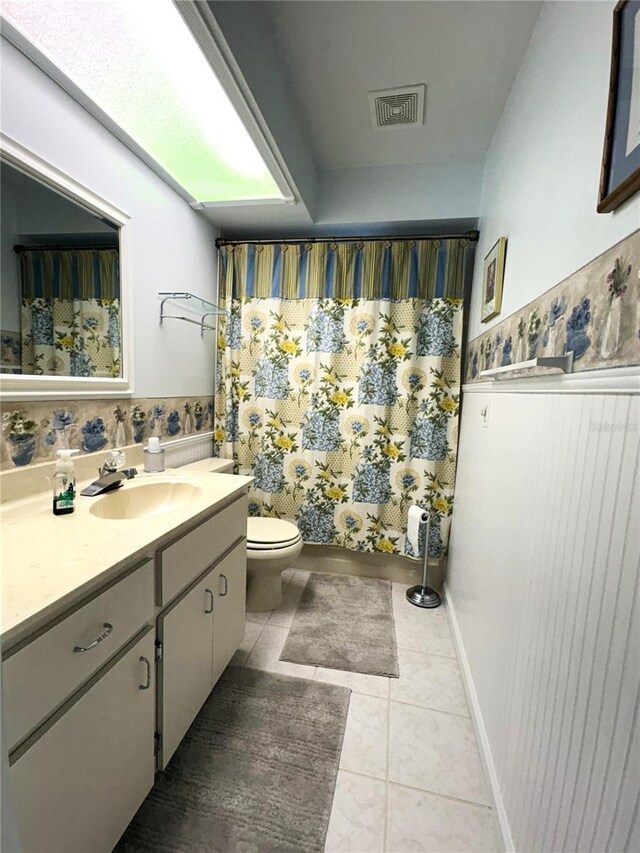 full bathroom with visible vents, vanity, tile patterned floors, a wainscoted wall, and toilet