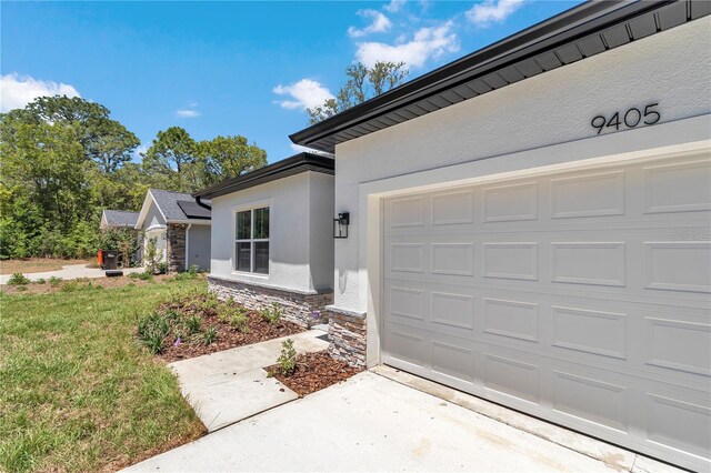 doorway to property featuring an attached garage, stone siding, stucco siding, concrete driveway, and a yard
