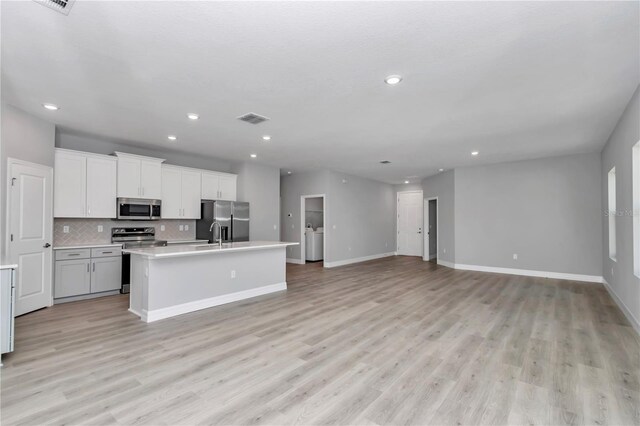 kitchen with decorative backsplash, a kitchen island with sink, appliances with stainless steel finishes, light wood finished floors, and open floor plan