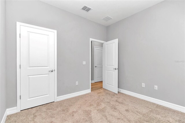 unfurnished bedroom with baseboards, light carpet, and visible vents