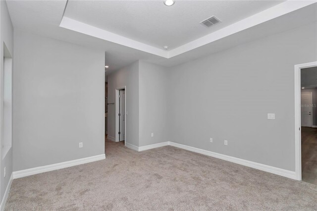 carpeted empty room featuring visible vents, a raised ceiling, and baseboards