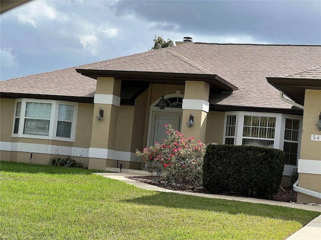 entrance to property featuring a yard, roof with shingles, and stucco siding