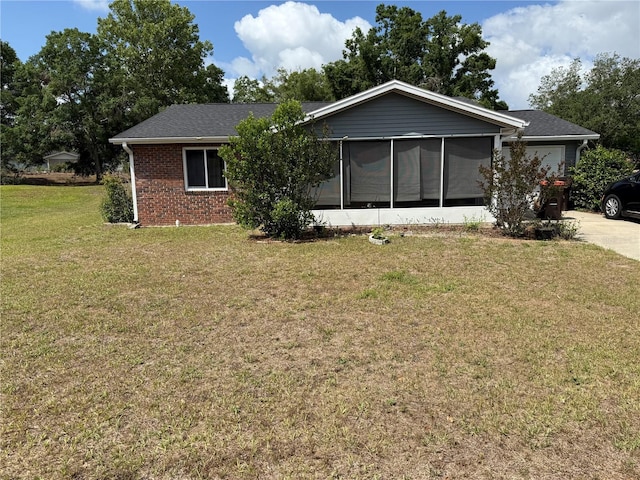back of property with driveway, a sunroom, a garage, brick siding, and a yard