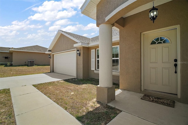 view of exterior entry featuring an attached garage, central AC unit, stucco siding, and driveway